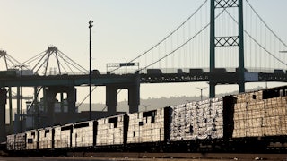 Loaded freight cars sit beneath a bridge.