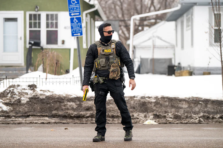 An ICE agent holds a taser while standing on the street, wearing a face mask.