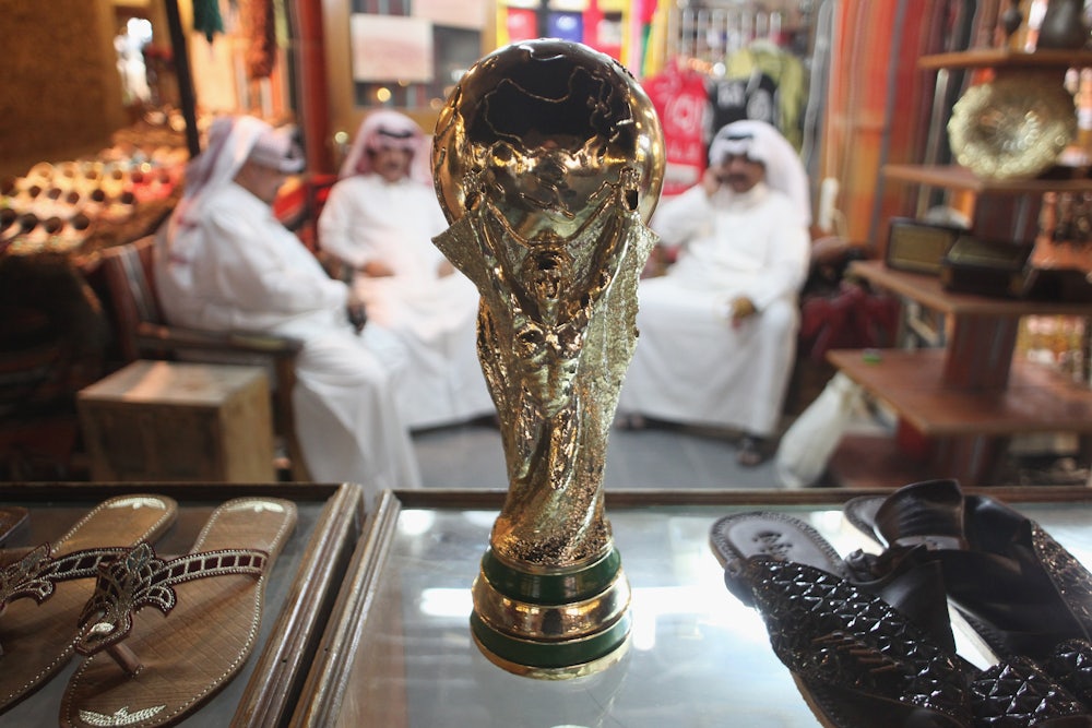 Men sit at a shoemaker's stall with a replica of the FIFA World Cup trophy in the Souq Waqif traditional market in Doha, Qatar.