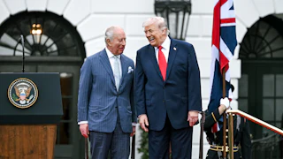 King Charles III and Donald Trump laugh while standing next to each other on a platform outside the White House