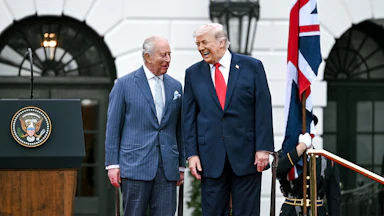 King Charles III and Donald Trump laugh while standing next to each other on a platform outside the White House