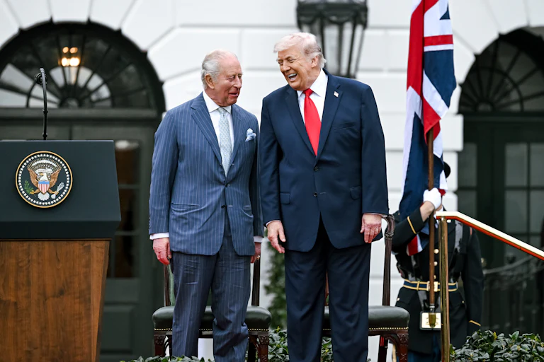 King Charles III and Donald Trump laugh while standing next to each other on a platform outside the White House