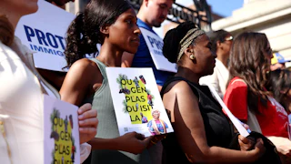 Community members hold signs of support written in Haitian Creole that translate to “You Belong Here” during a press conference held in the wake of the Supreme Court decision to overturn TPS for Haitians and Syrians outside of the State House on June 25, 2026.