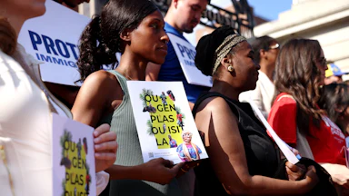 Community members hold signs of support written in Haitian Creole that translate to “You Belong Here” during a press conference held in the wake of the Supreme Court decision to overturn TPS for Haitians and Syrians outside of the State House on June 25, 2026.