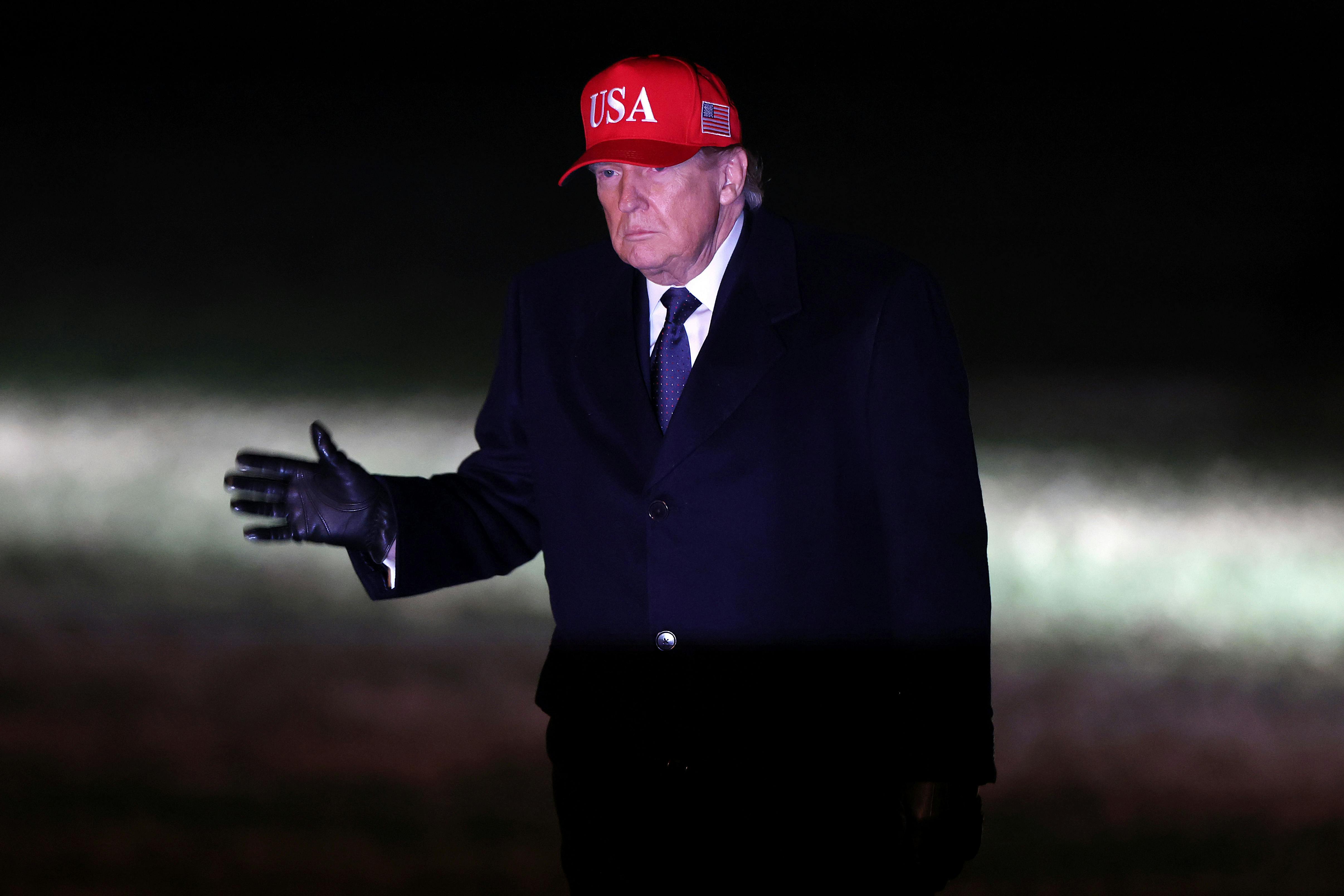 Donald trump walks in the dark wearing a red usa hat 