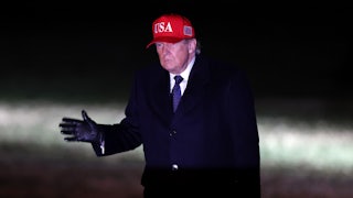 Donald trump walks in the dark wearing a red usa hat