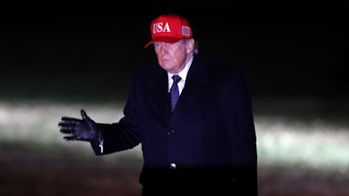 Donald trump walks in the dark wearing a red usa hat