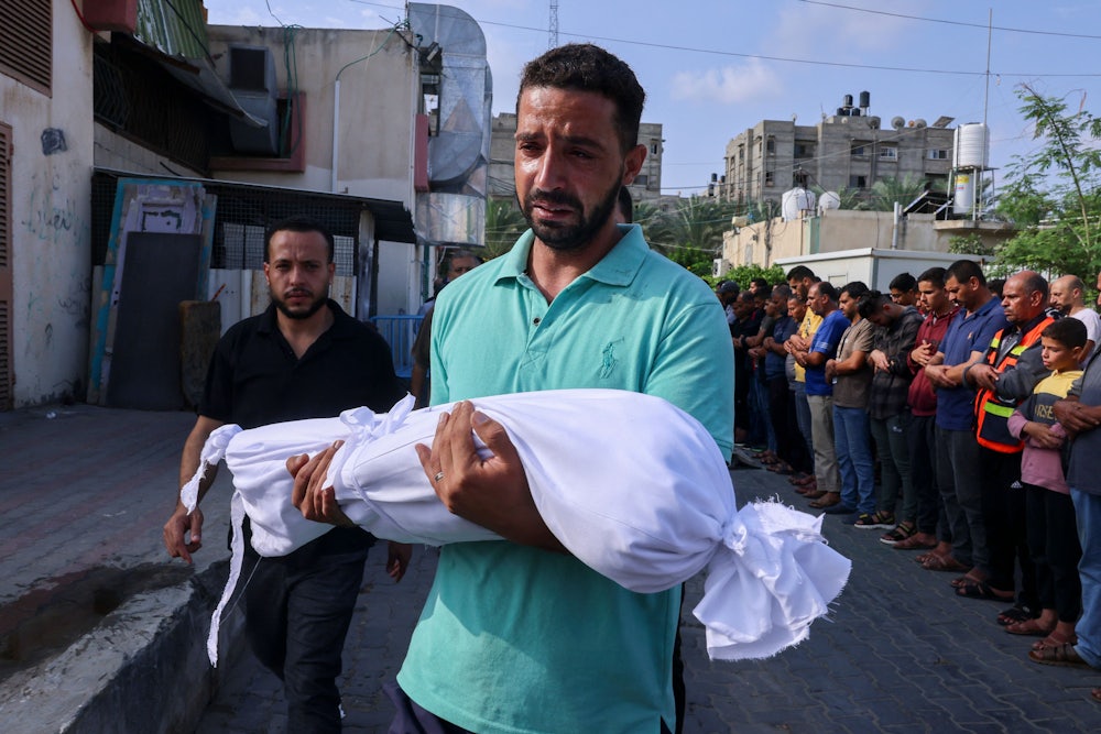 A Palestinian man carries the body of a child killed in Israeli shelling