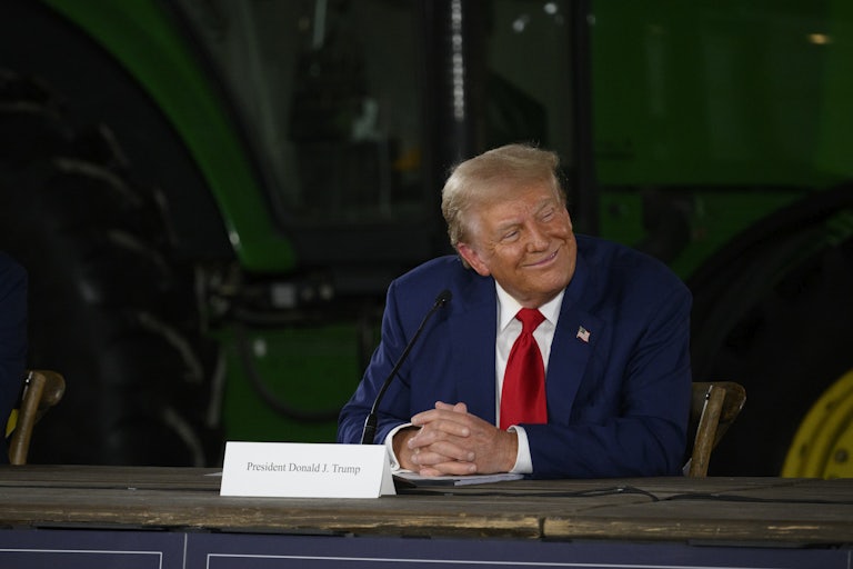 Donald Trump smiles while seated at a table during a campaign event