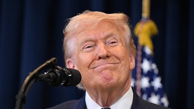 Donald Trump smiles while standing in front of a microphone