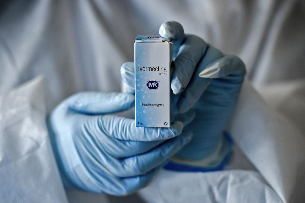 Gloved hands hold a box of Ivermectin.