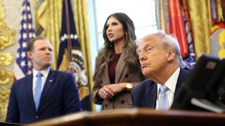 Donald Trump sits at the desk in the Oval Office, with Kristi Noem and Andrew Giuliani behind him.