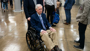 Senator Mitch McConnell sits in a wheelchair being pushed through the Senate subway
