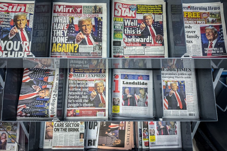 A newsstand displays headlines from The Sun, The Mirror, Daily Star, The Times, and more reporting Trump's election victory.