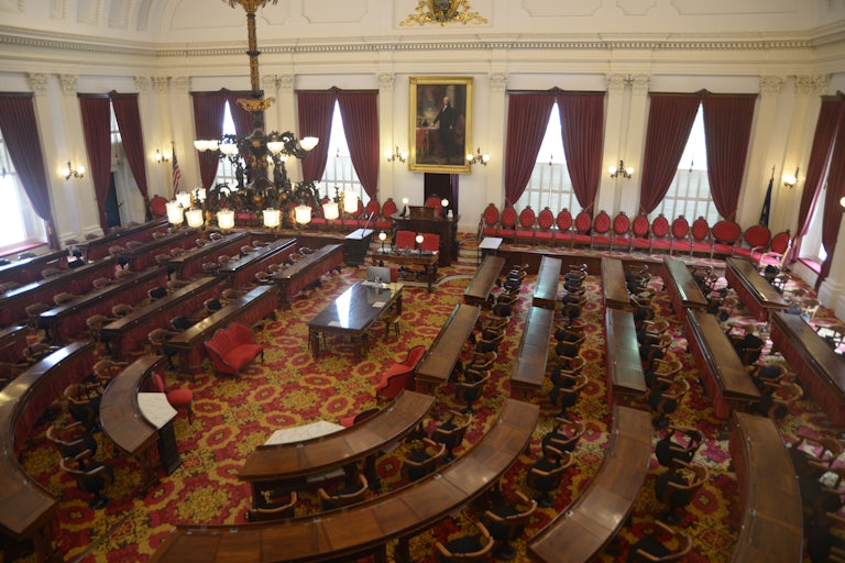 The photo depicts Vermont's empty House of Representatives room.