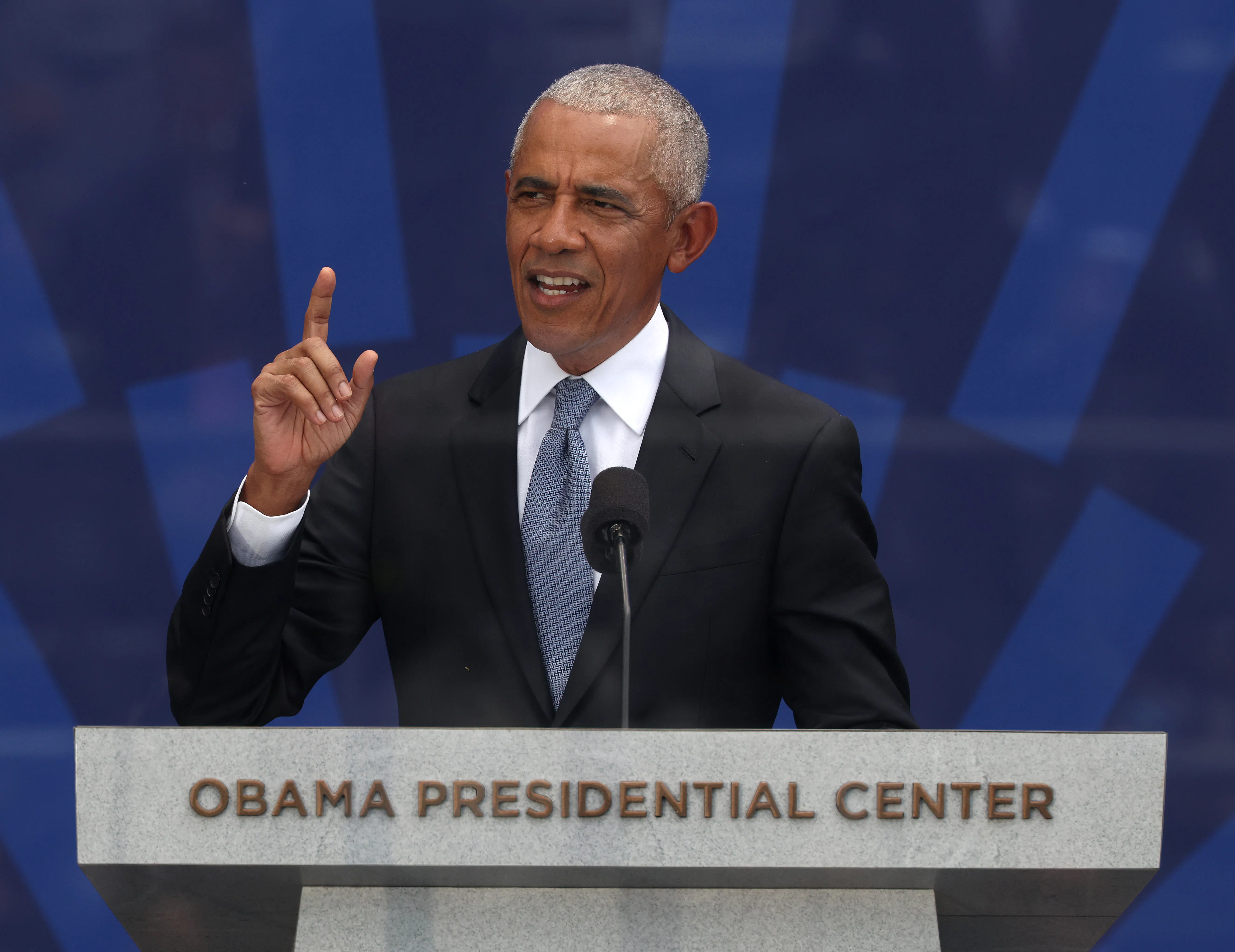 Barack Obama holds his right index finger in the air while speaking