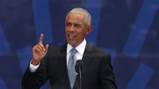 Barack Obama holds his right index finger in the air while speaking