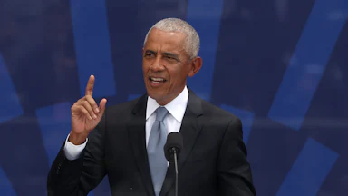 Barack Obama holds his right index finger in the air while speaking