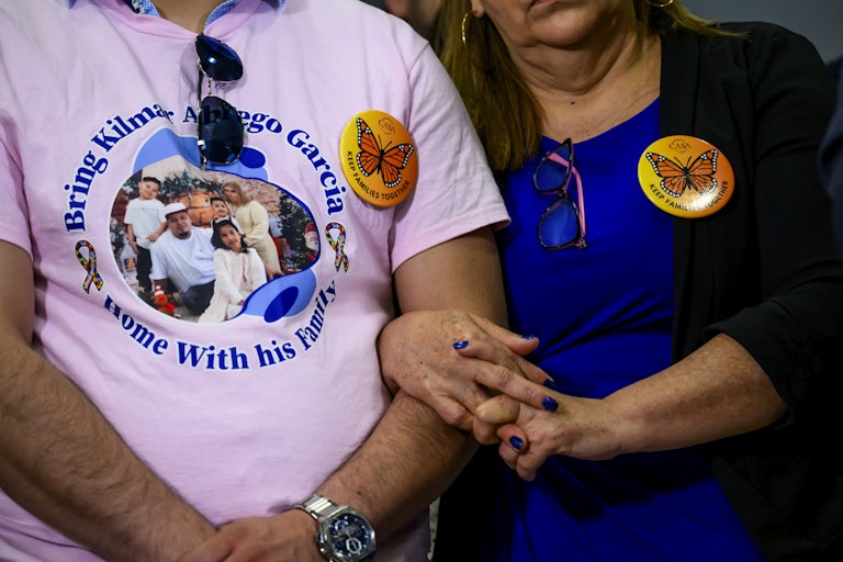 Kilmar Abrego Garcia's brother and mother stand next to each other with their arms linked during a press conference by Senator Chris Van Hollen. Abrego Garcia's brother wears a shirt calling for Abrego Garcia's return