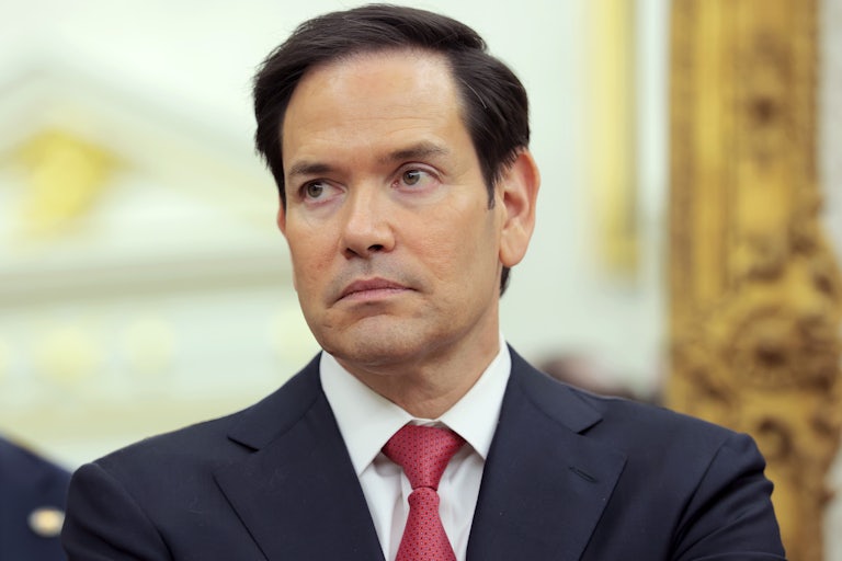 Marco Rubio wears a suit and red tie and stares blankly