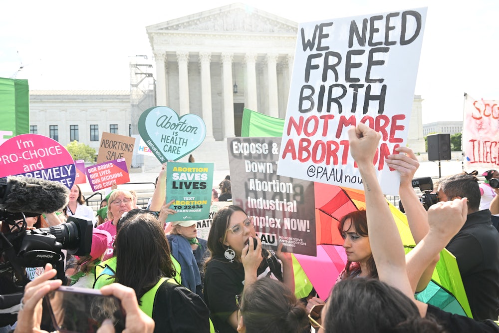 Demonstrators hold colorful signs with the Supreme Court building in the background.