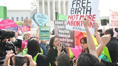 Demonstrators hold colorful signs with the Supreme Court building in the background.
