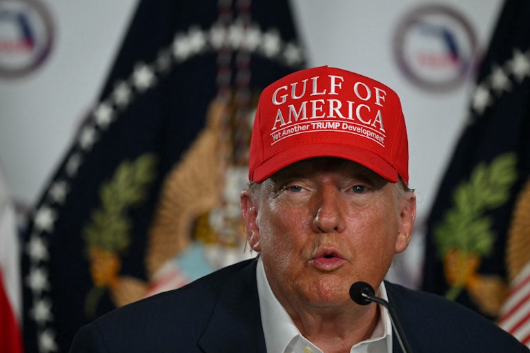 Donald Trump wears a "Gulf of America" hat and puckers his lips while speaking to reporters at "Alligator Alcatraz"