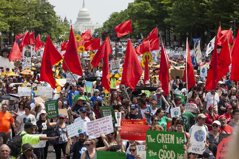 Protesters fill the streets in front of the Capitol, holding signs and waving red flags.