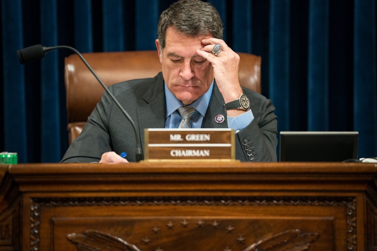 Representative Mark Green sitting in a hearing, holding his hand to his forehead and looking down.