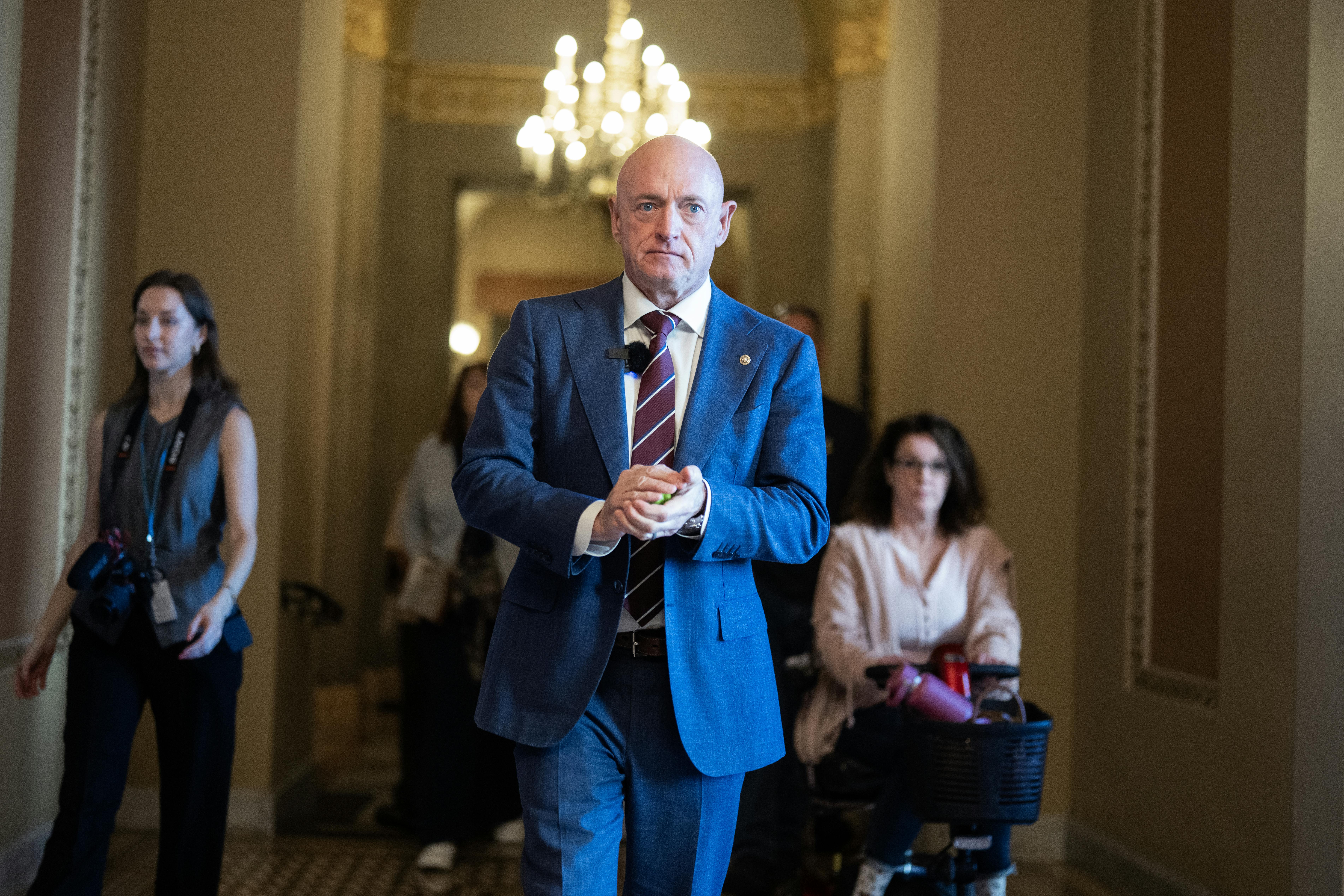 Senator Mark Kelly puts his hands together while walking in the Capitol