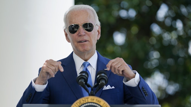 Joe Biden, wearing sunglasses, points downward towards his podium.