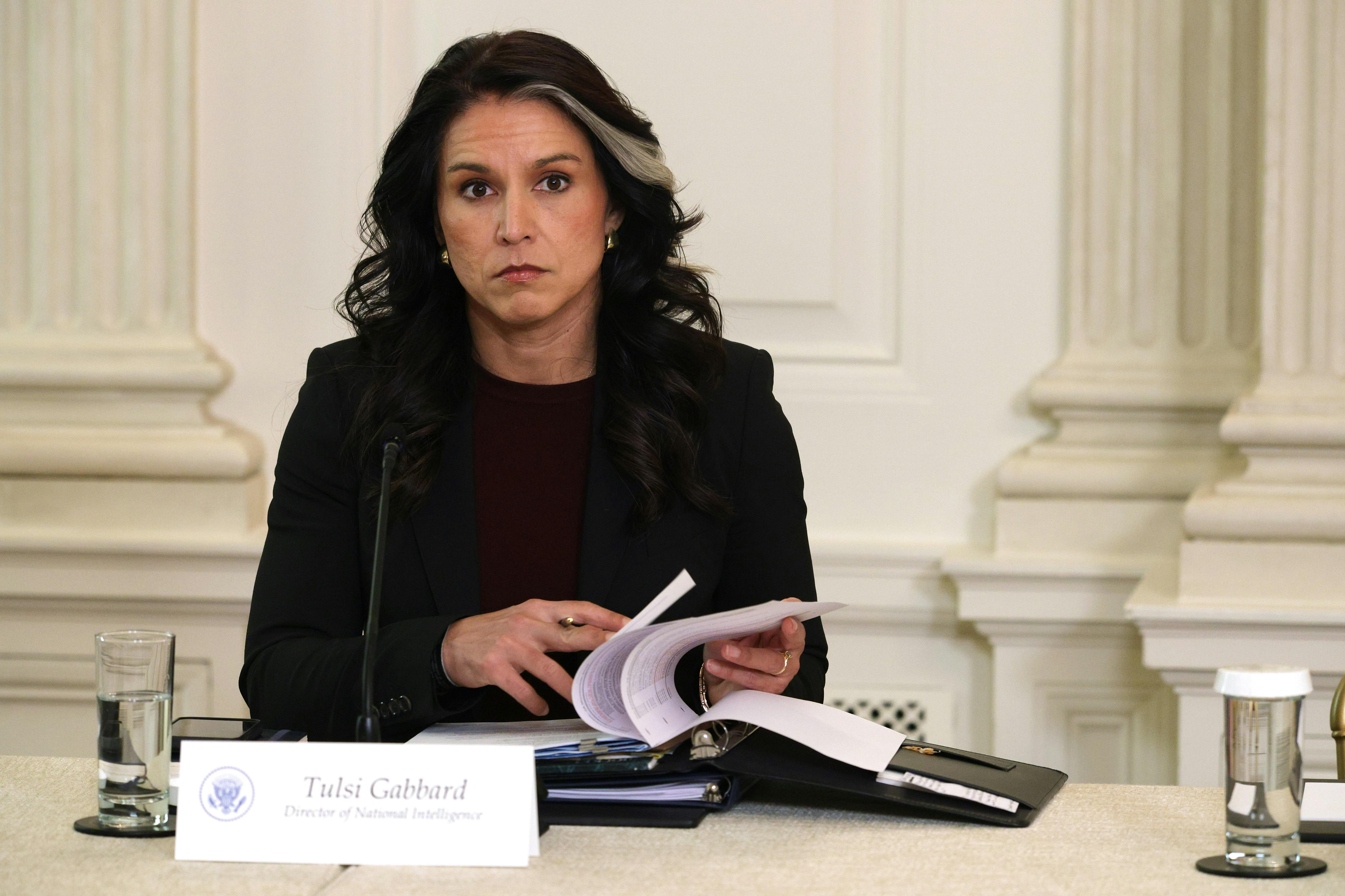 Director of National Intelligence Tulsi Gabbard sits at a table and turns pages in a binder