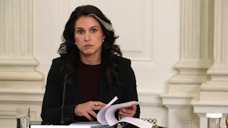 Director of National Intelligence Tulsi Gabbard sits at a table and turns pages in a binder