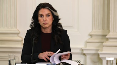 Director of National Intelligence Tulsi Gabbard sits at a table and turns pages in a binder