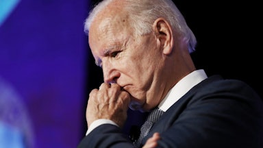A close up of President Joe Biden, scowling into his fist.