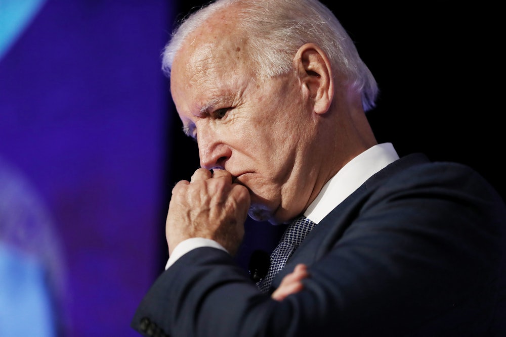 A close up of President Joe Biden, scowling into his fist.