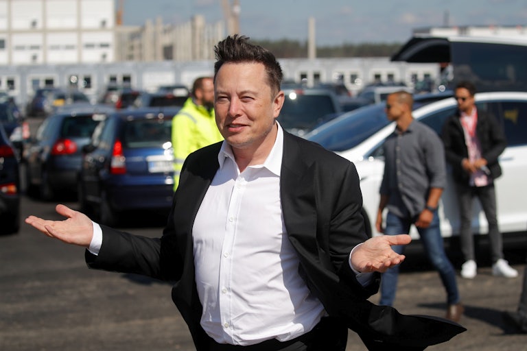 Elon Musk gestures in front of a group of cars.