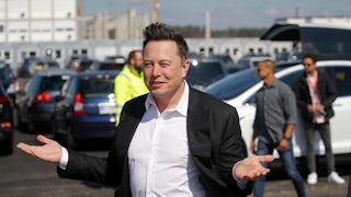 Elon Musk gestures in front of a group of cars.