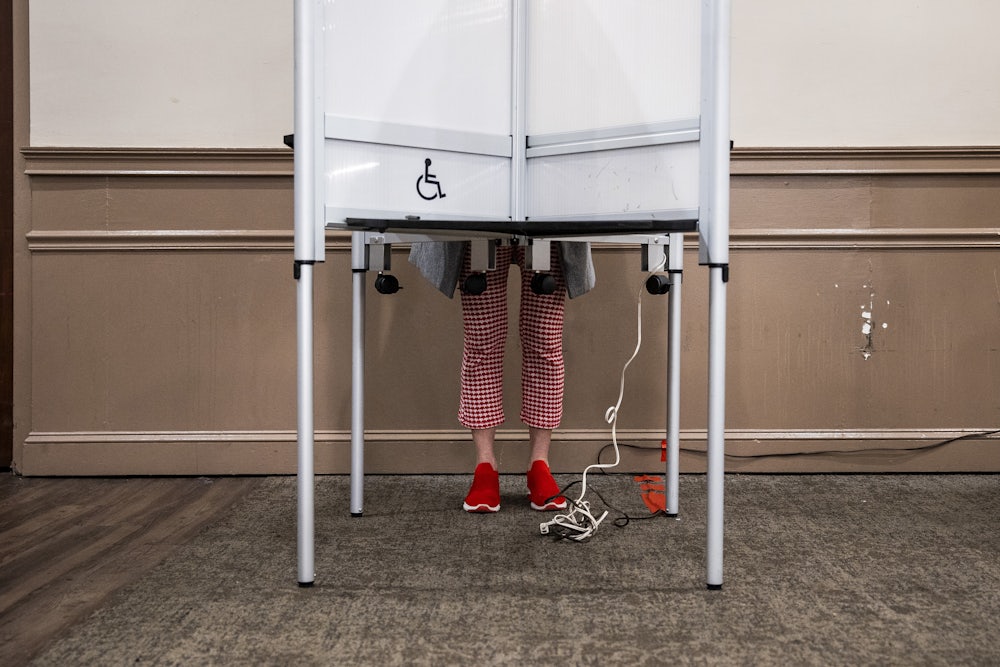 This image shows a person’s legs and feet visible beneath the polling booth as they cast their vote.