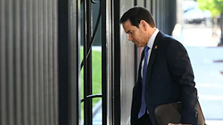 Secretary of State Marco Rubio walks into a building with a folder in his hand.