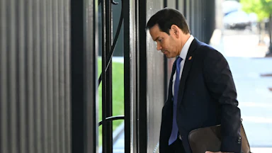 Secretary of State Marco Rubio walks into a building with a folder in his hand.