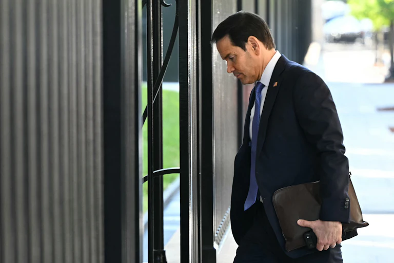 Secretary of State Marco Rubio walks into a building with a folder in his hand.