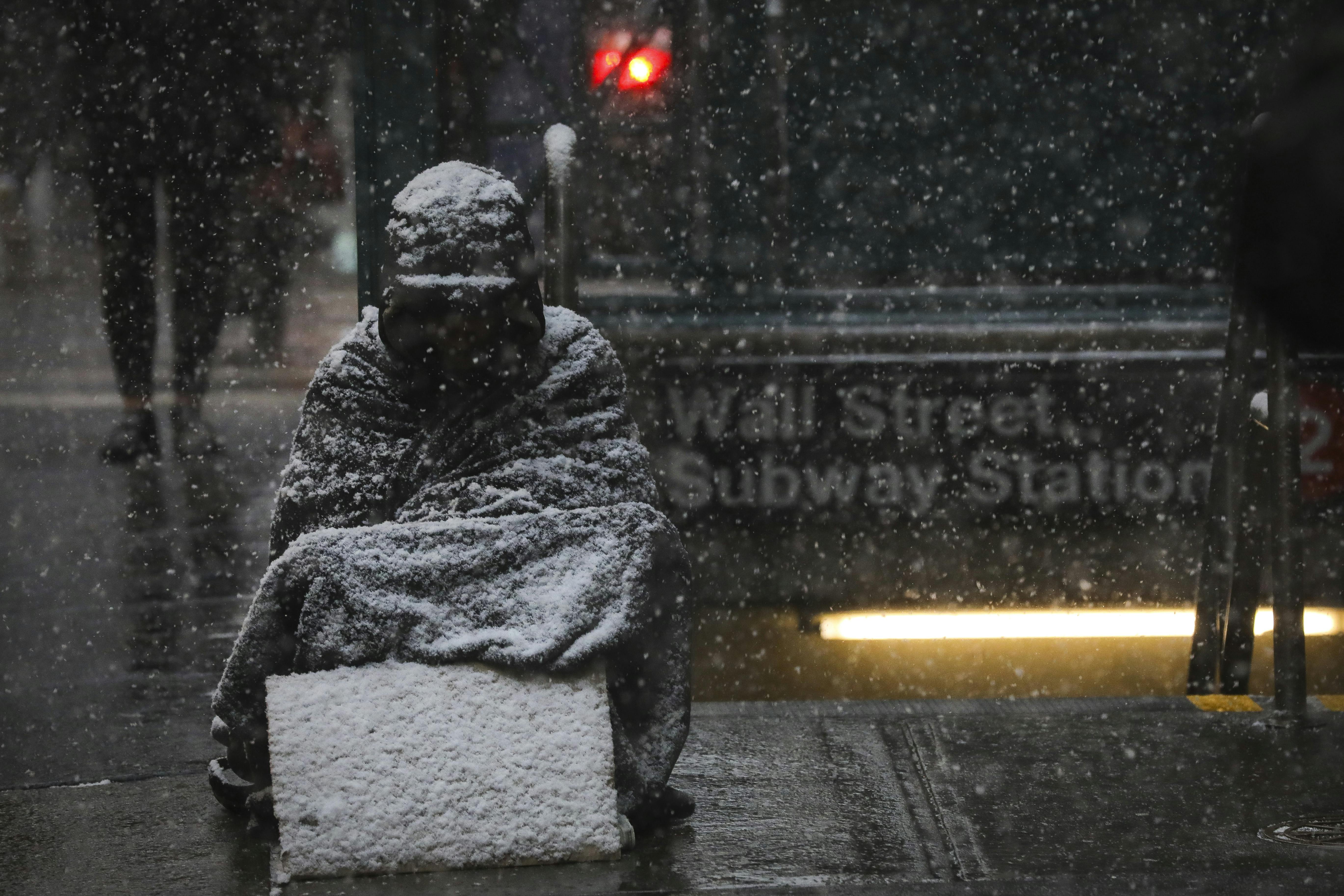A homeless man sits in the falling snow in New York’s financial district 