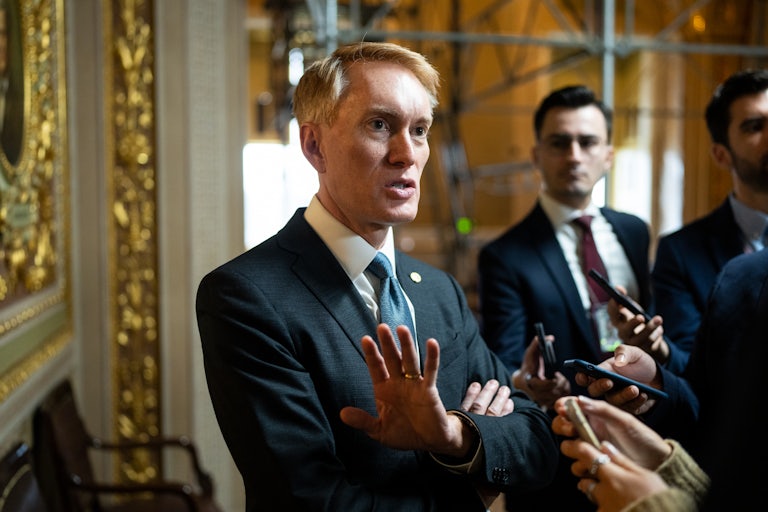 James Lankford is speaking and holds his hand up. Several hands in front of him hold phones to record his speech.