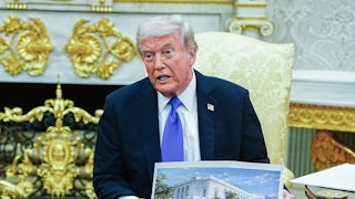 Donald Trump speaks and holds up renderings of his ballroom while sitting in the Oval Office