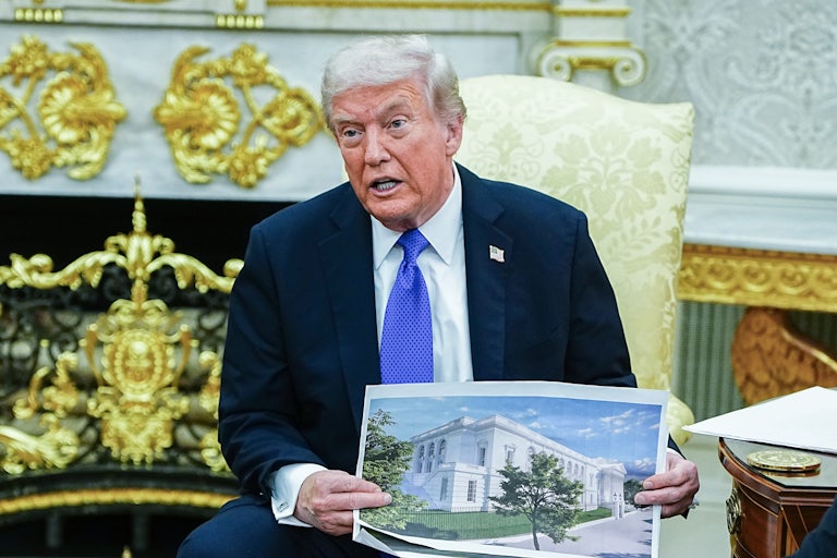 Donald Trump speaks and holds up renderings of his ballroom while sitting in the Oval Office