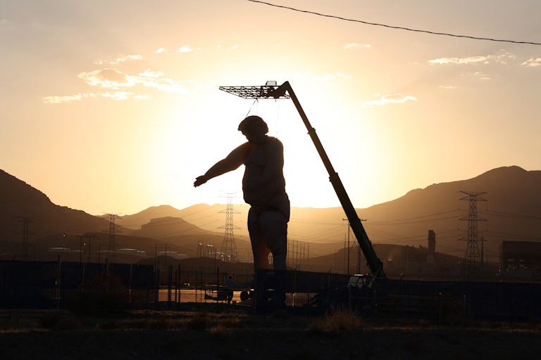 The giant nude Trump statue, darkened because of the sun in the background