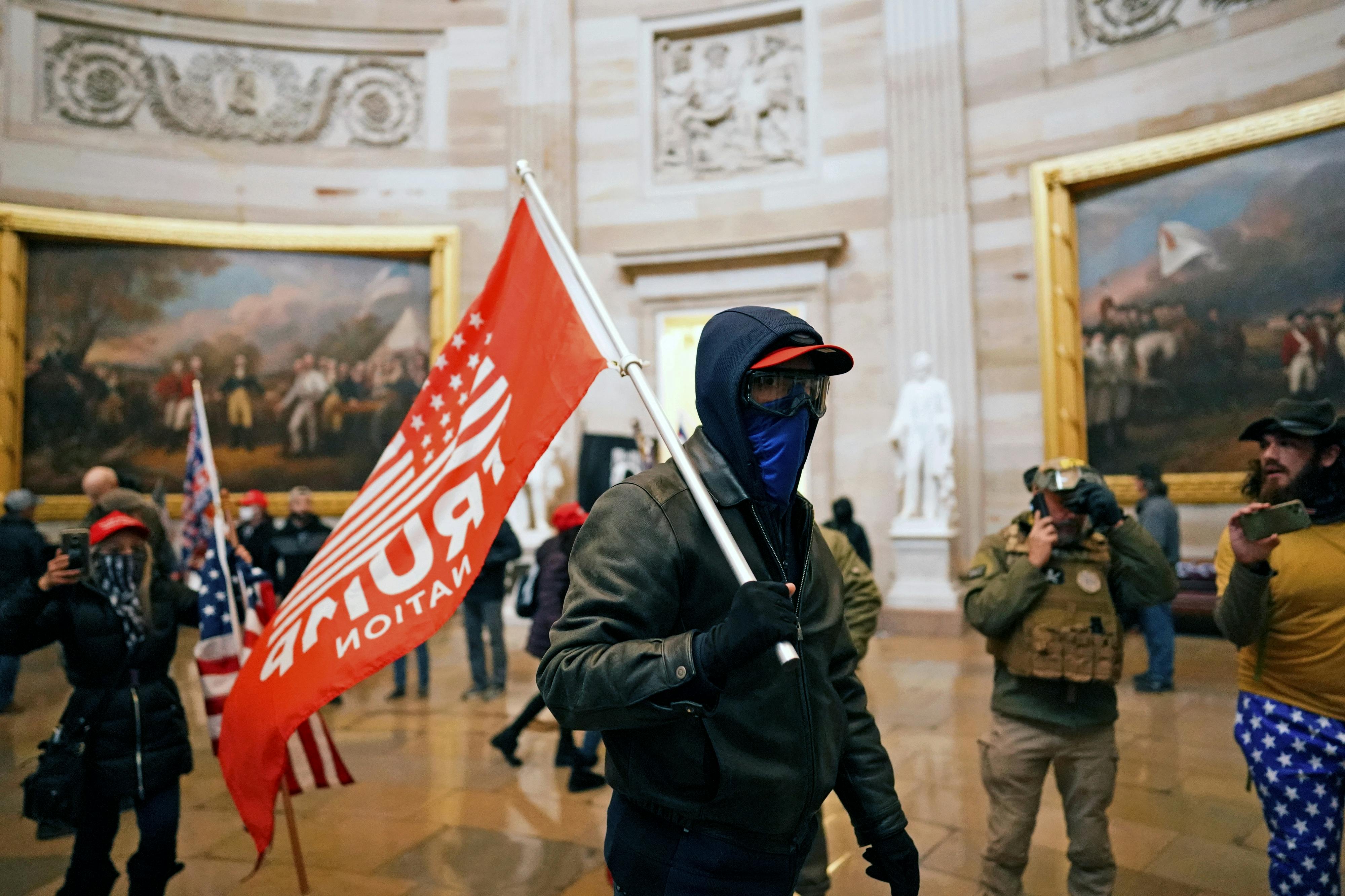 A masked January 6 rioter waves a large red Trump flag inside the Capitol.