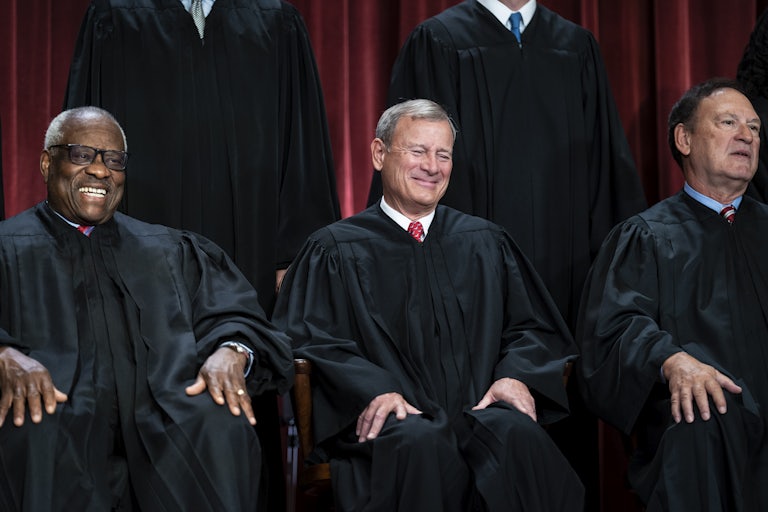 Supreme Court Justices Clarence Thomas and John Roberts smile, wearing their robes. Samuel Alito, sitting next to them, is zoning out.