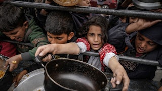 Palestinian children, holding empty pots, wait in line to receive food prepared by volunteers for Palestinian families displaced to Southern Gaza due to Israeli attacks, between rubbles of destroyed buildings in Rafah, Gaza on February 10, 2024.